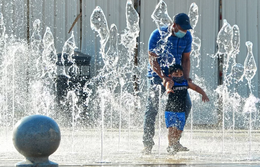 在科威特首都科威特城，一名父亲带着孩子在高温天气下的喷泉里玩耍